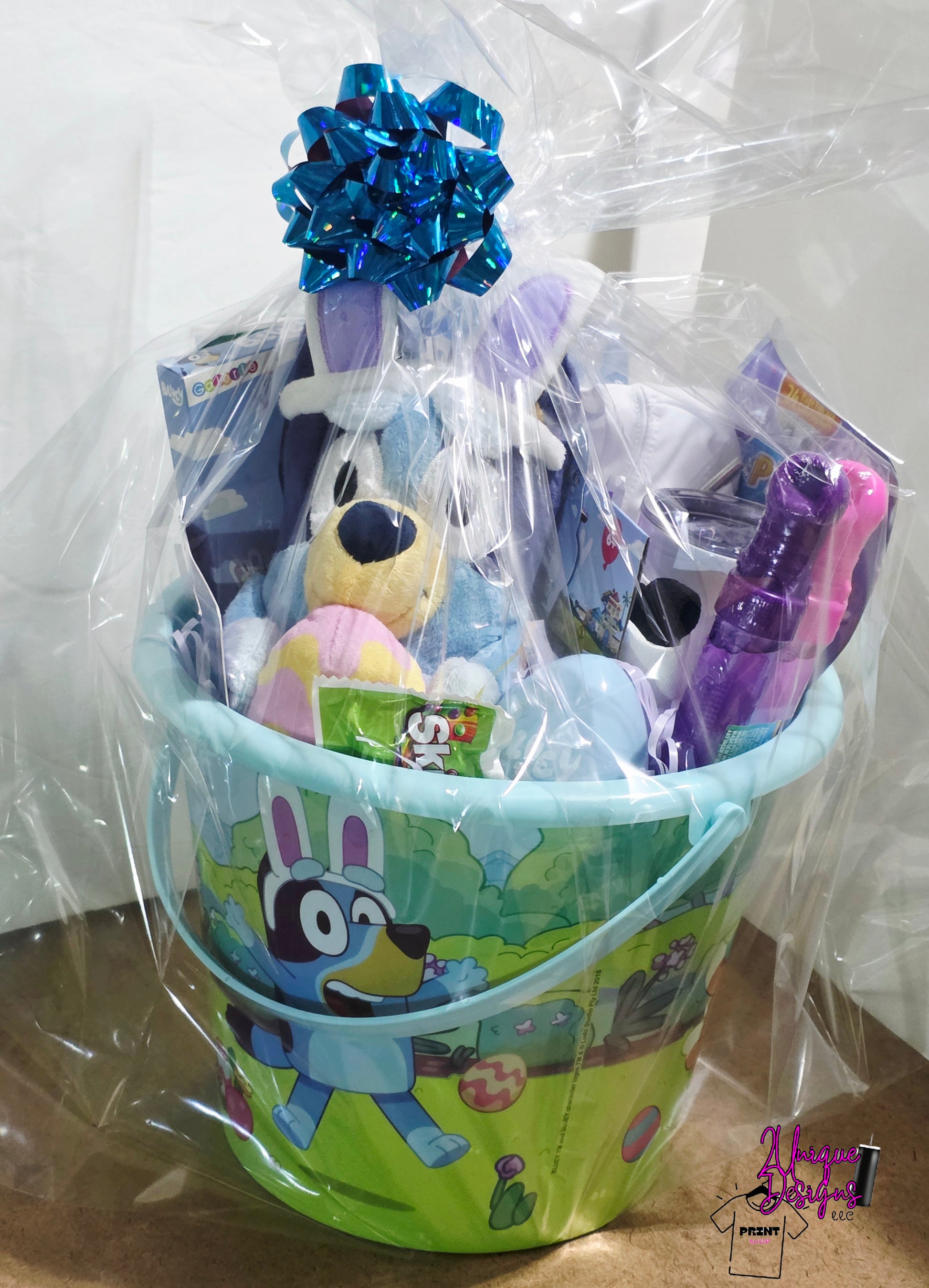 Gift basket with toys and a blue ribbon in a green bucket on a white background